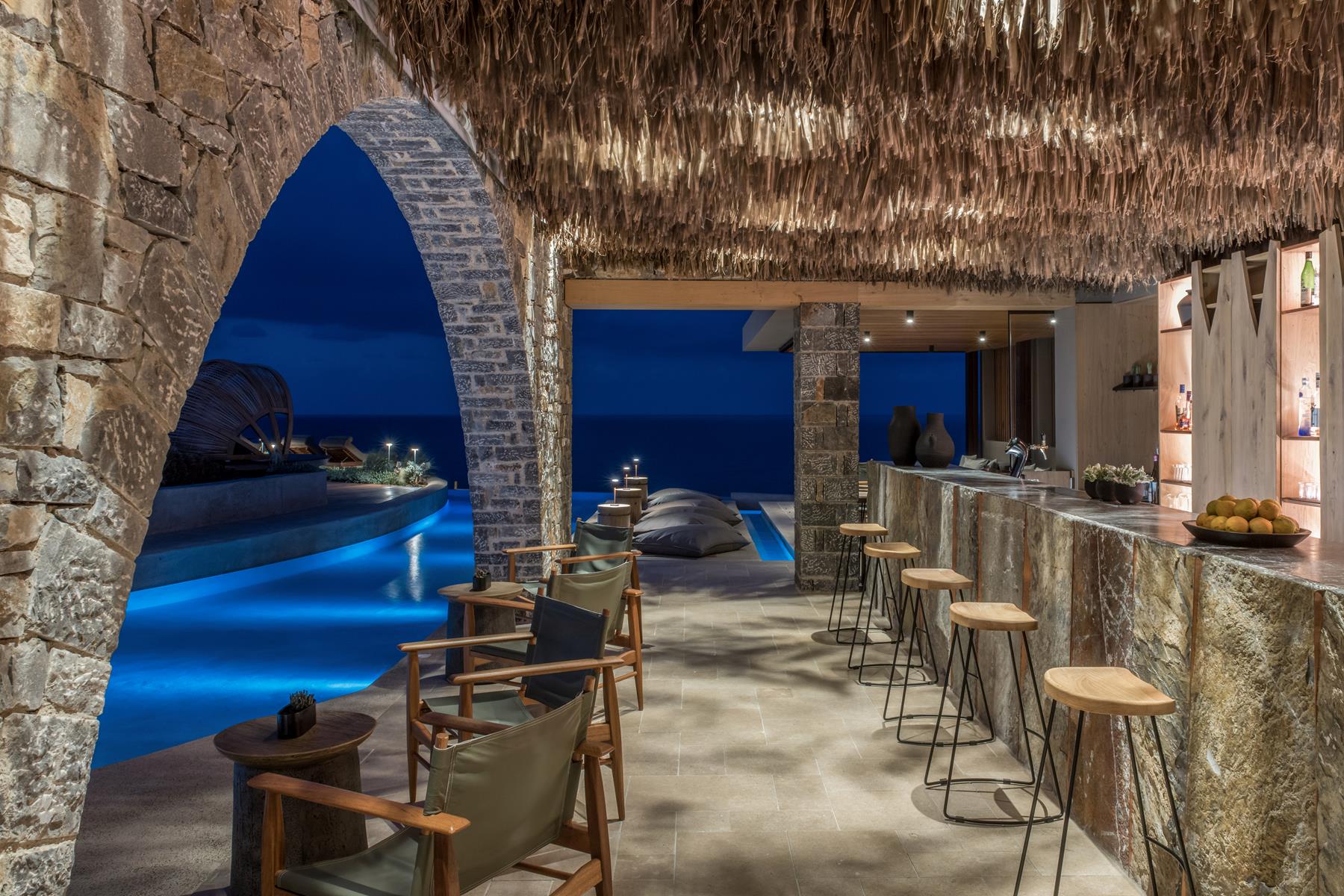The Circle pool bar at Acro Suites by night, thatched roof, stone arch and the lit pool beyond