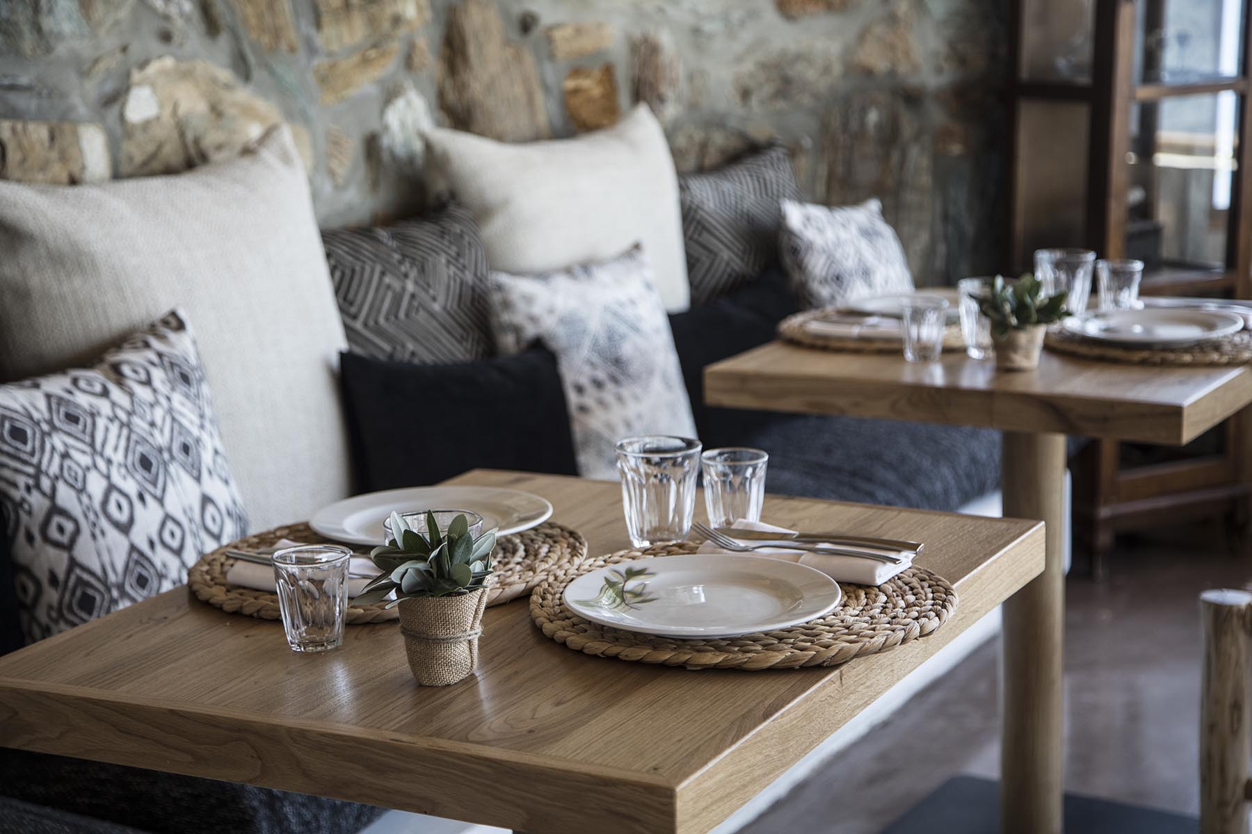 The Minoan taverna at Sea Side, rustic timber tables with woven placemats and cushions against a Cretan stone wall