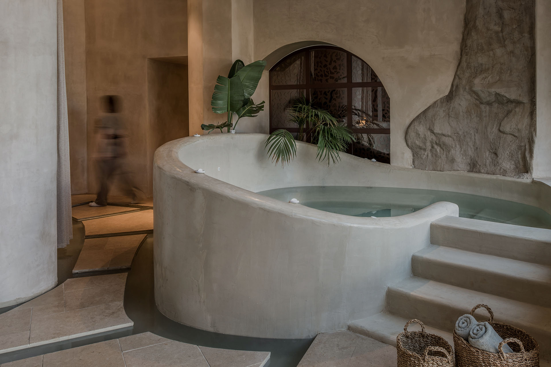 The curved plaster pool of the Bath House with stone arch and warm candlelight