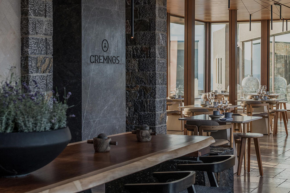 The Cremnos restaurant at Acro Suites, stone walls, warm timber tables and sea views through tall glass