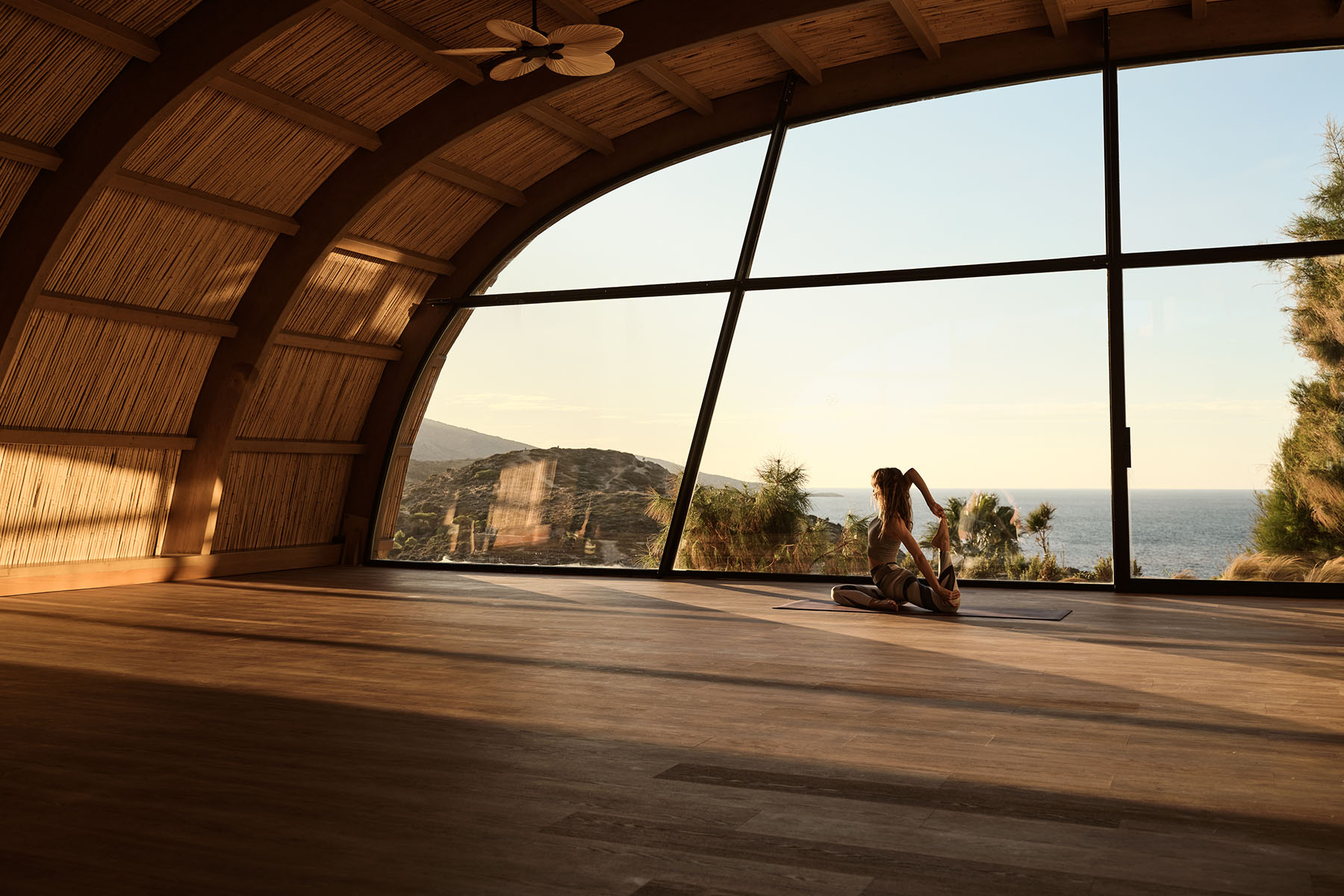 A guest practising yoga in the arched wooden Asana shala with the Cretan sea beyond the glass