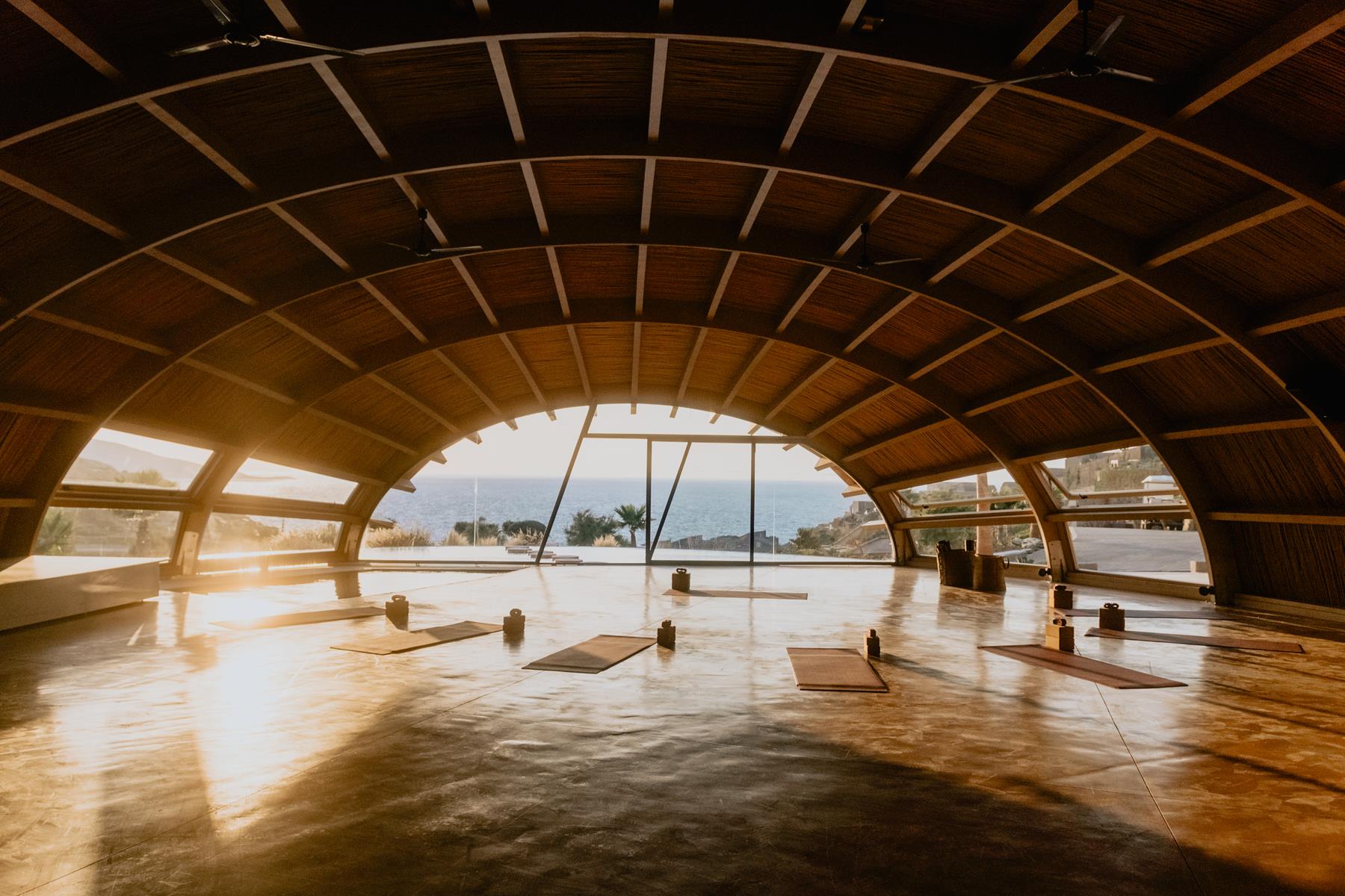The bamboo vaulted ceiling of the Asana yoga studio at golden hour, mats laid out for practice